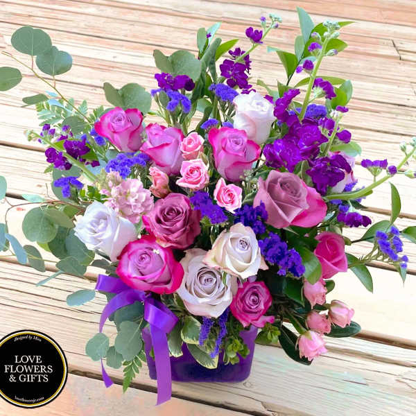Mixed bouquet of pink and lavender roses with purple flowers in a purple vase