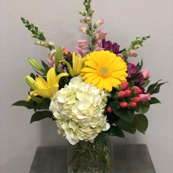 Mixed bouquet with yellow lilies, white hydrangea, and pink flowers in a glass vase