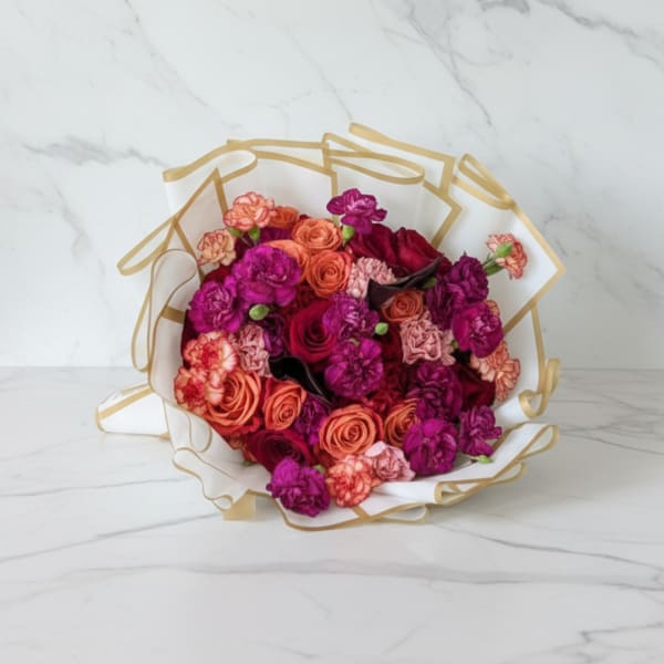 Bouquet of pink, coral, and purple roses wrapped in white paper with gold trim
