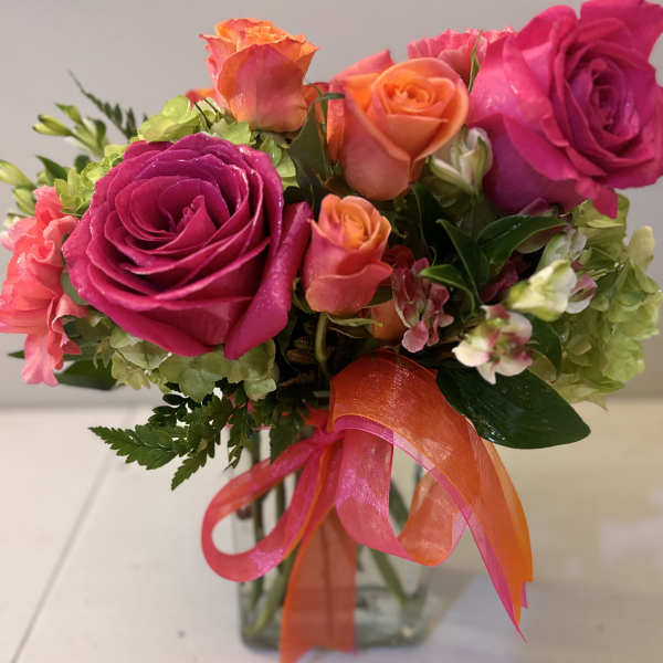 Pink and orange roses in a glass vase with a ribbon bow