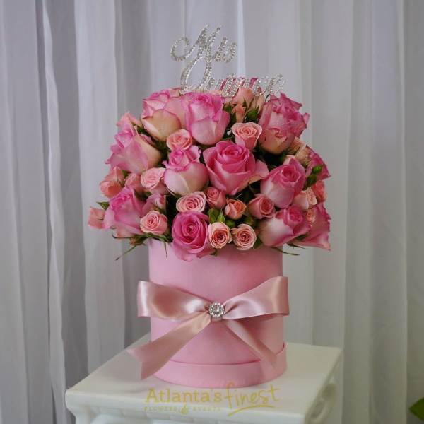 Pink roses arranged in a round pink hatbox with a satin bow