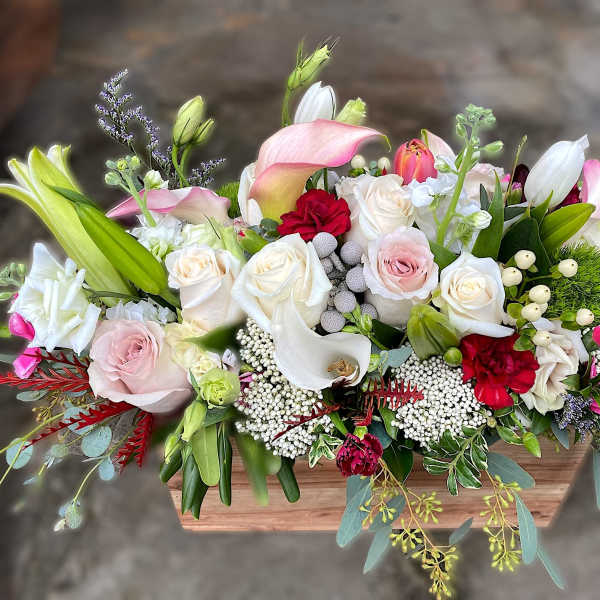 Low wooden box arrangement with white and pink roses, calla lilies, lilies, and red accent flowers