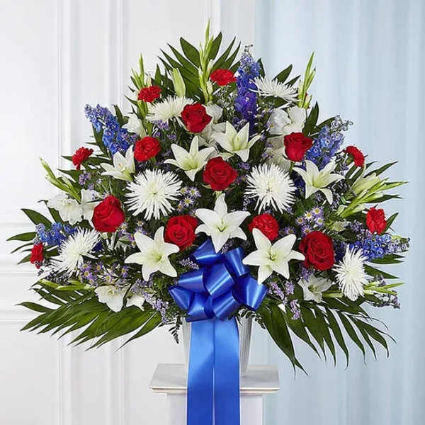 Large standing floral spray with red roses, white lilies, and blue accents