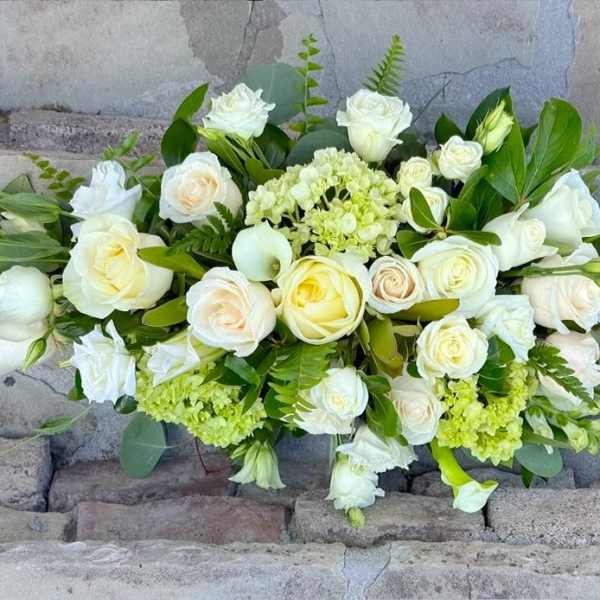 Low arrangement of white and cream roses with soft green blooms in an elongated design