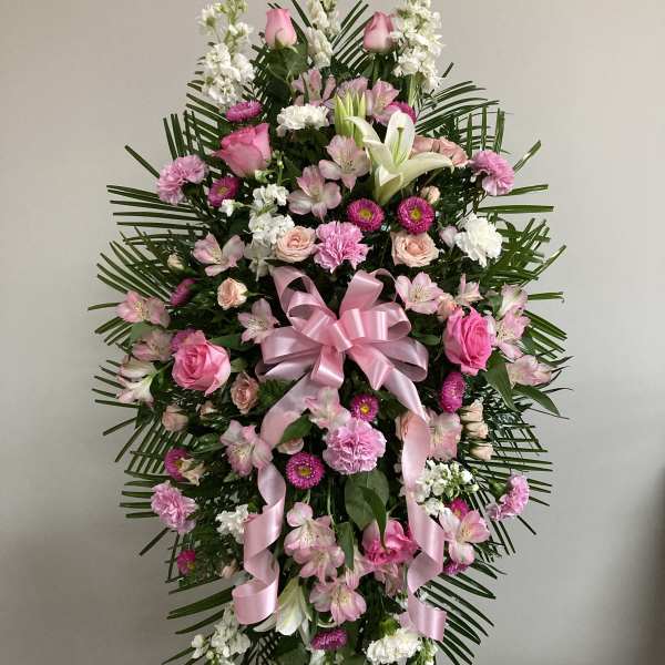 Pink and white funeral spray with roses, lilies, and ribbon