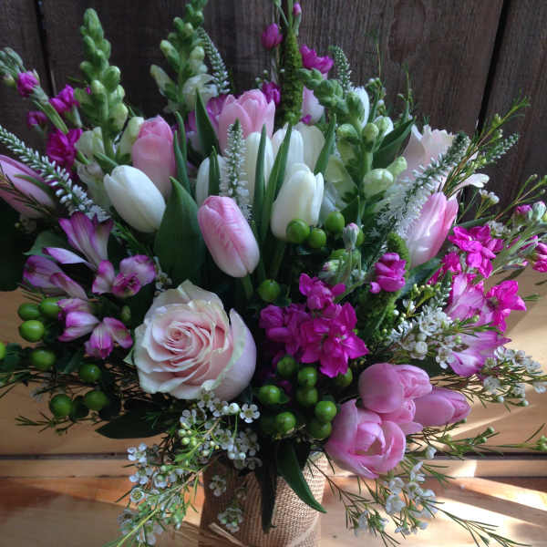 Bouquet of pink and white tulips, roses, and purple flowers in a burlap-wrapped vase