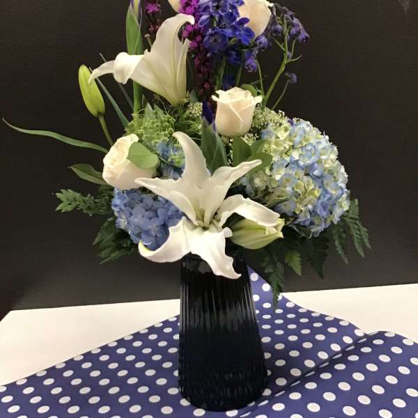 White lilies and blue hydrangeas in a black vase