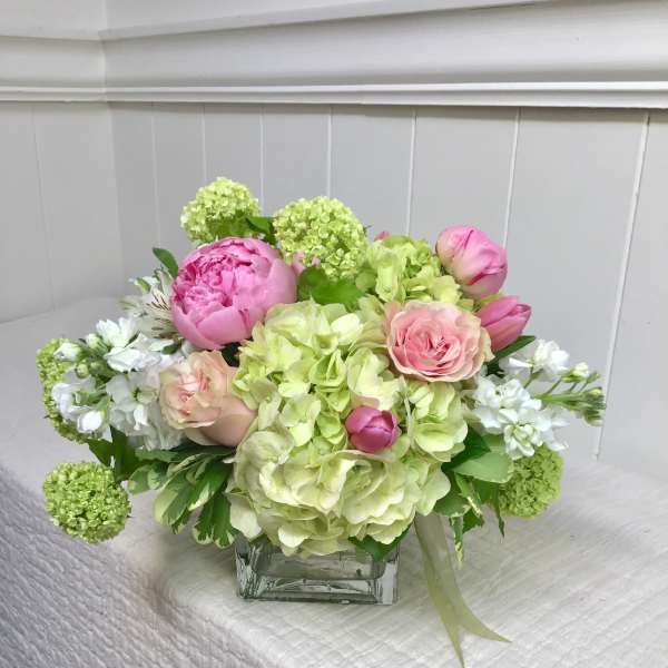 Pink peonies and roses arranged with green hydrangeas in a glass vase