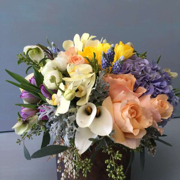Mixed bouquet of peach, purple, white, and yellow flowers in a dark vase