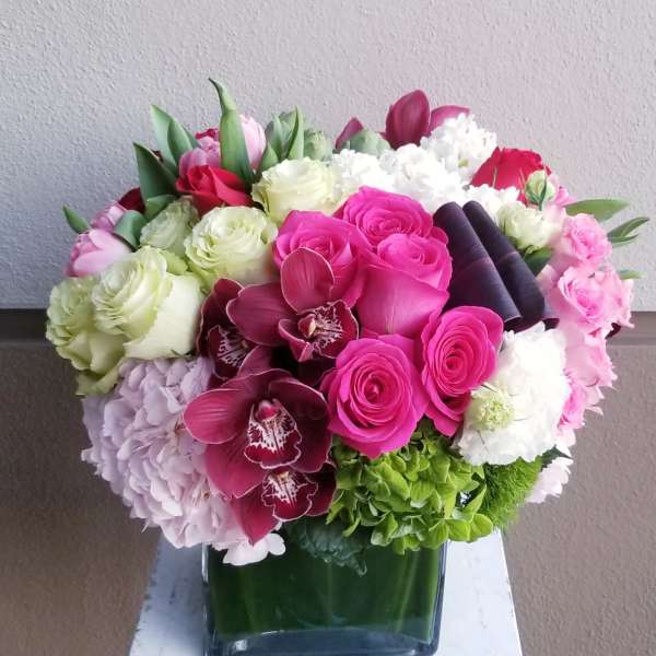 Mixed bouquet of pink, white, and green flowers in a square glass vase