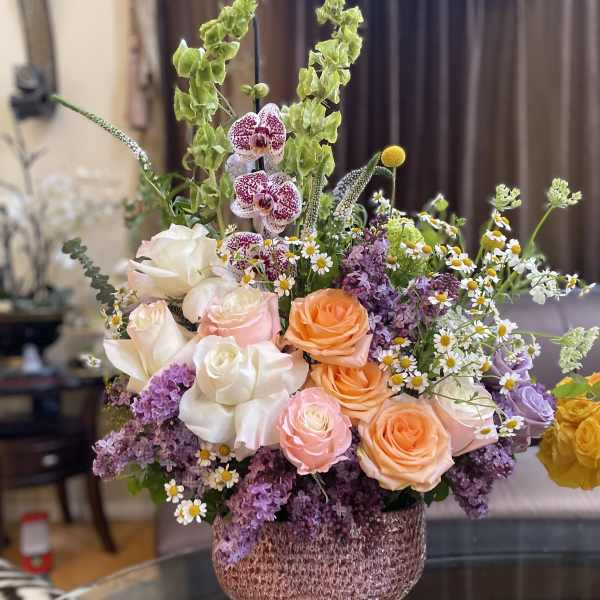 Mixed bouquet of roses, orchids, and small daisies in a textured vase