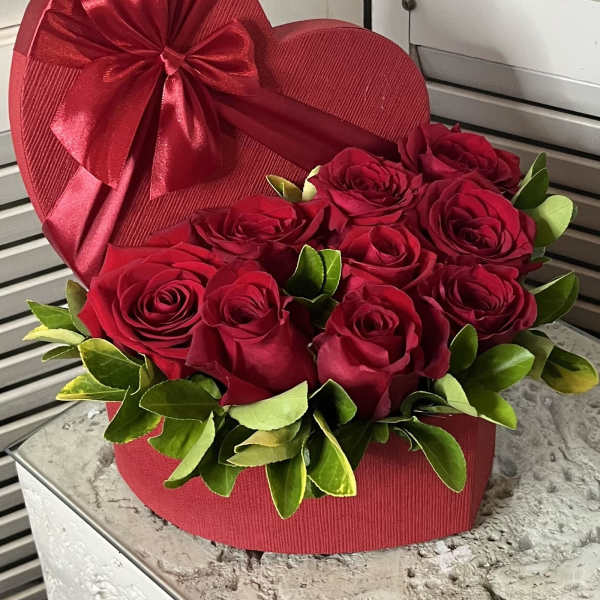 Red roses arranged in a heart-shaped box with a satin bow