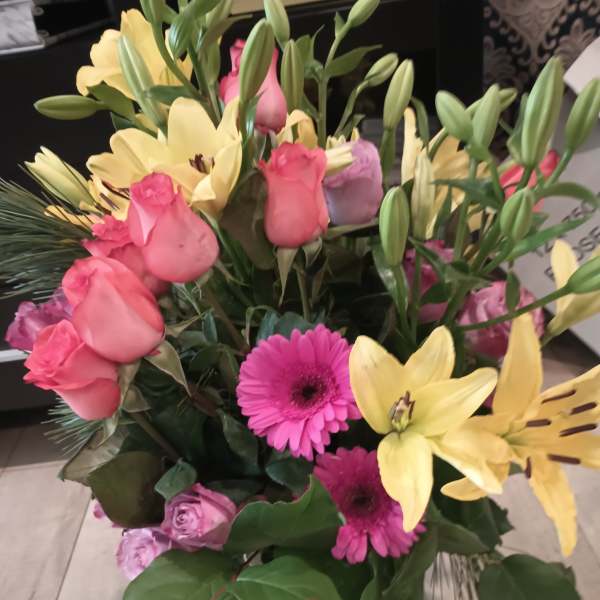 Mixed bouquet of pink roses, yellow lilies, and pink gerbera daisies in a glass vase