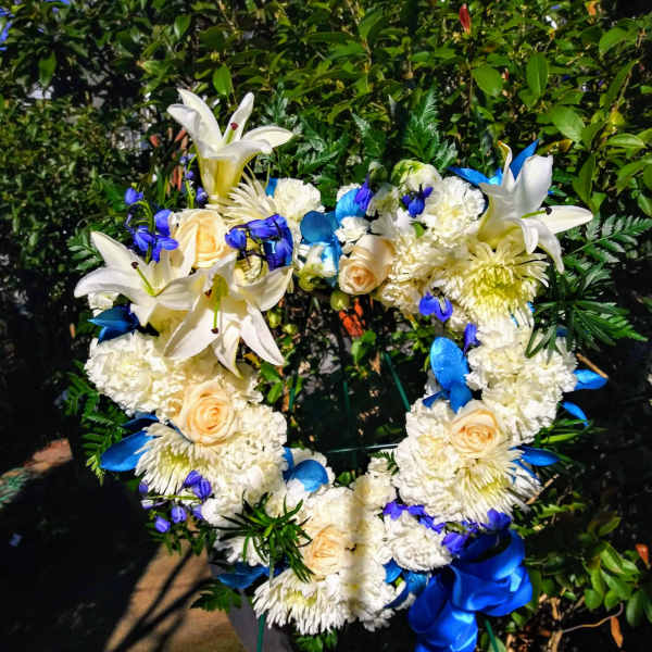 Heart-shaped floral wreath with white lilies, cream roses, and blue ribbon accents
