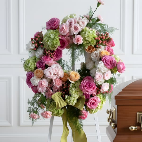 Pink and green floral wreath on a stand beside a casket
