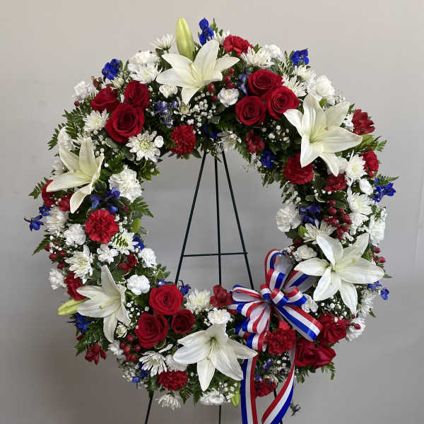 Circular wreath of red, white, and blue flowers on a stand with a ribbon bow