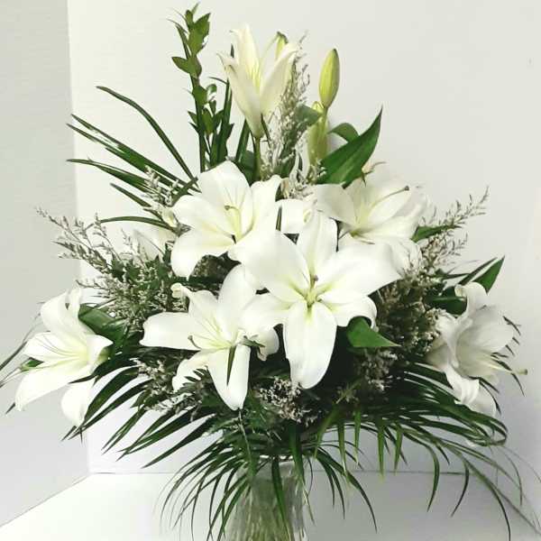 White lilies arranged in a clear glass vase with greenery