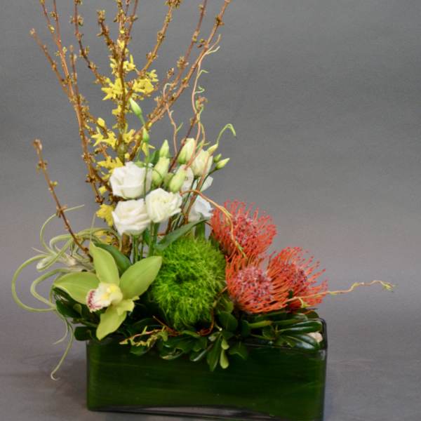 Tall floral arrangement with white blooms, yellow accents, and red pincushion flowers in a green vase