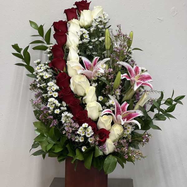 Tall arrangement of red and white roses with pink lilies in a wooden vase