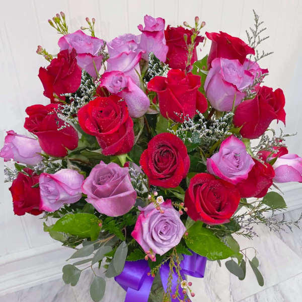 Arrangement of red and lavender roses in a clear vase with a purple ribbon bow