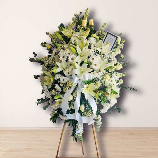 White floral standing spray on an easel with a ribbon bow