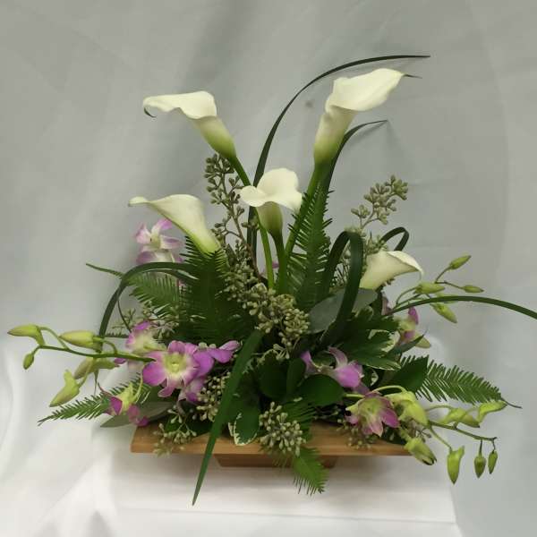 White calla lilies and purple orchids in a low wooden container