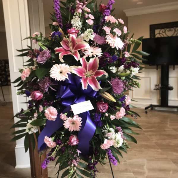 Large standing floral spray with pink lilies and purple flowers on a ribboned easel