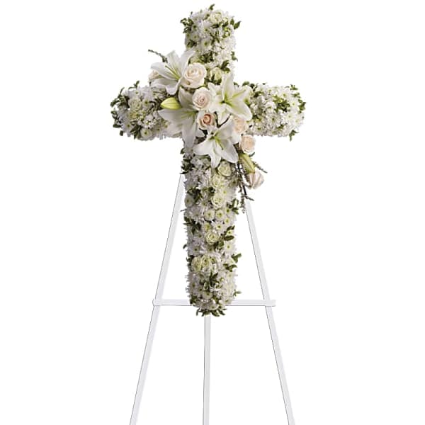 White floral cross on a stand with lilies and roses