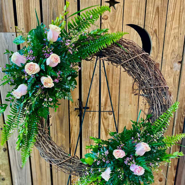 Floral crescent wreath with pale pink roses and greenery on a stand