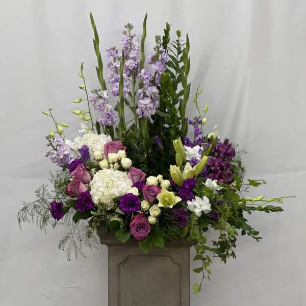 Tall floral arrangement with purple, white, and pink blooms in a pedestal container