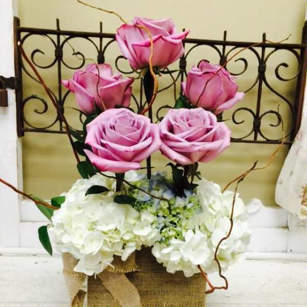Pink roses arranged above white hydrangeas in a burlap-wrapped container