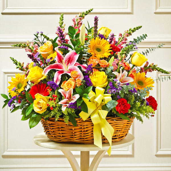 Bright mixed basket with yellow roses, pink lilies, red carnations and other flowers with a yellow bow