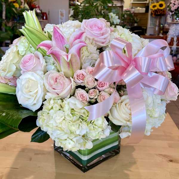 Pink and white floral arrangement with lilies, roses, and hydrangeas in a square vase