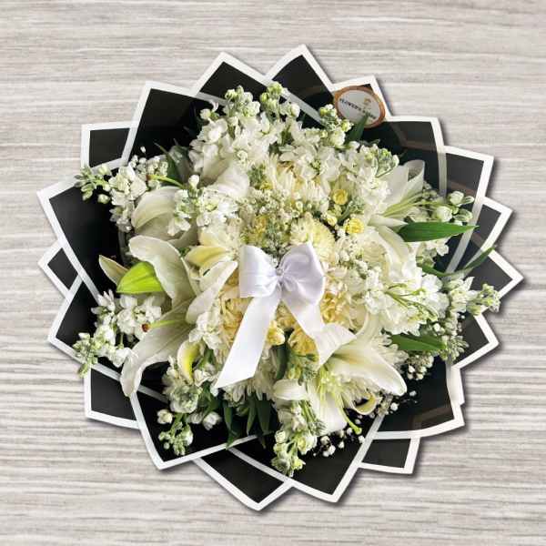 White floral bouquet with lilies and a satin bow on black wrap