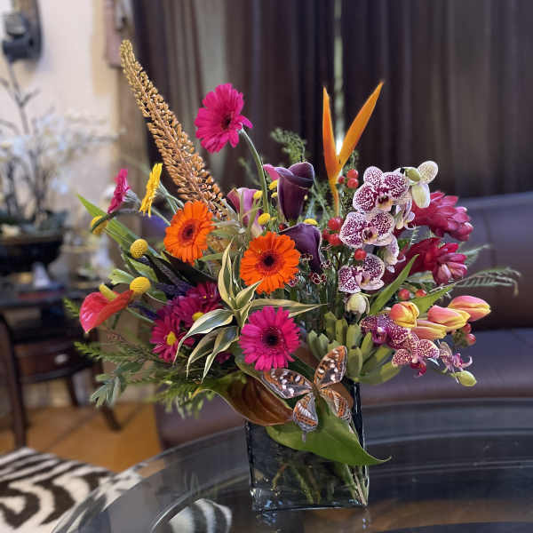 Colorful mixed bouquet in a square glass vase with orchids and gerbera daisies