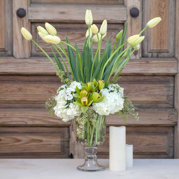 White tulips and hydrangeas in a clear glass vase with two candles