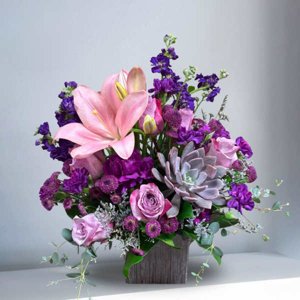 Pink lilies and roses with purple flowers in a wooden vase