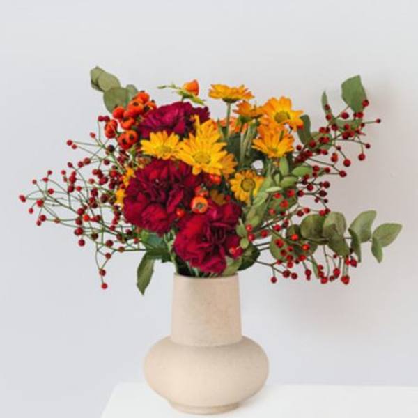 Bright mixed bouquet in a beige vase with red berries