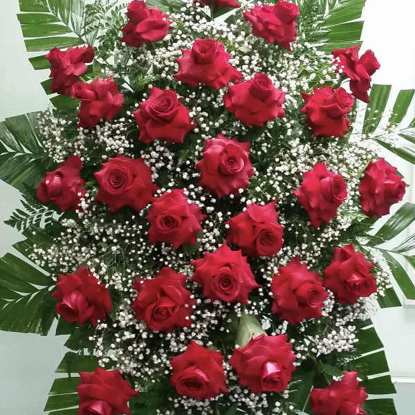 Standing spray of red roses with white filler and large tropical leaves
