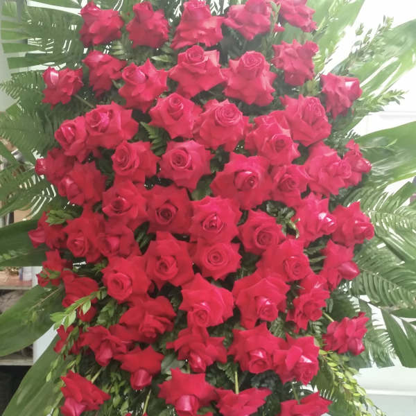 Large standing arrangement of red roses with tropical greenery