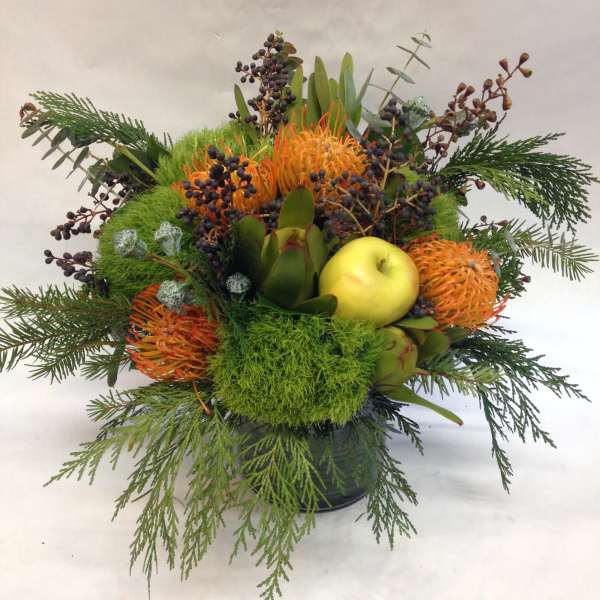 Mixed floral arrangement with orange blooms and a yellow apple in a black container