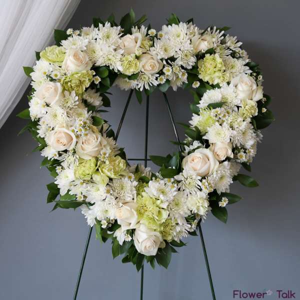 Heart-shaped floral wreath with white roses and chrysanthemums on a stand