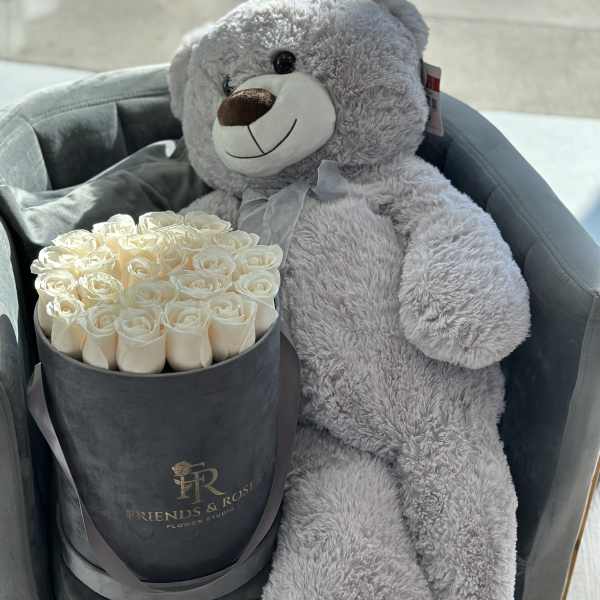 Cream roses in a black box beside a gray teddy bear