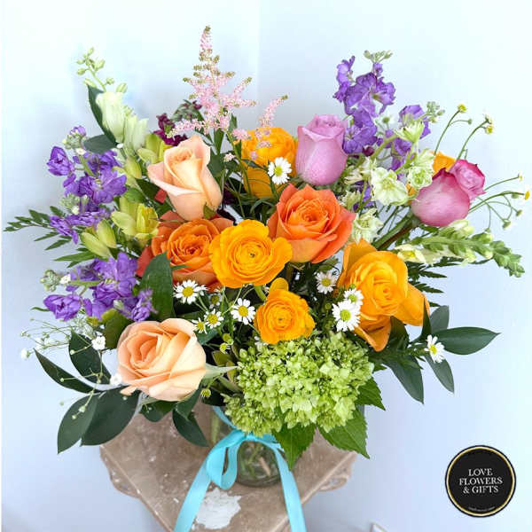 Bright mixed bouquet of orange and peach roses, yellow blooms, purple flowers and white daisies in a glass vase