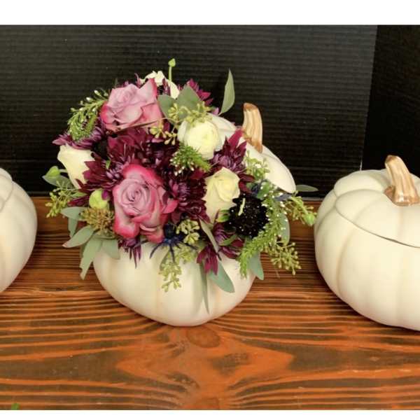 Floral arrangement in a white pumpkin container flanked by two matching pumpkins