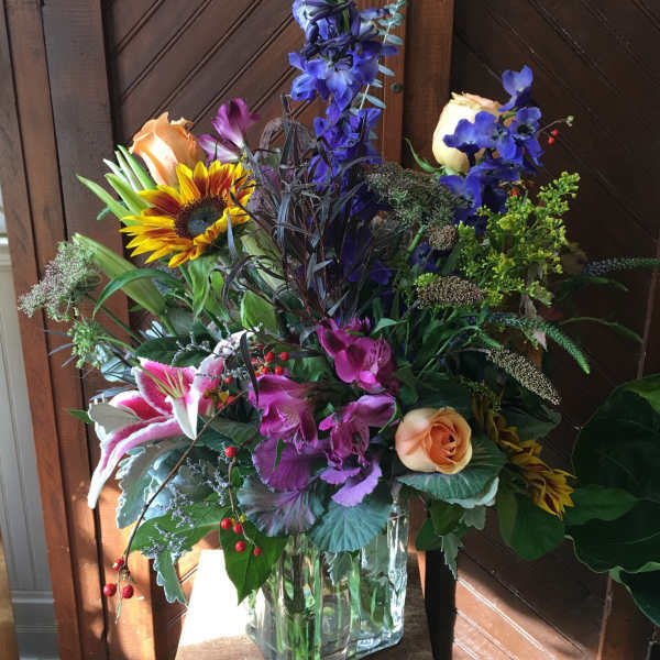 Mixed bouquet in a clear glass vase with roses, lilies, and a sunflower