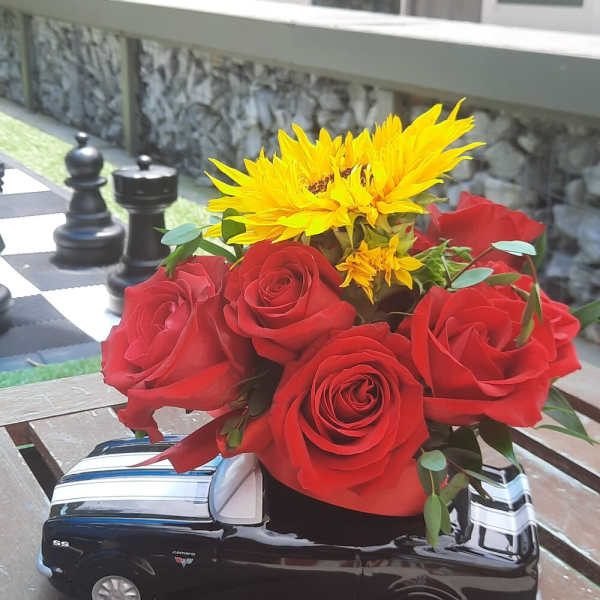 Red roses and yellow sunflowers arranged in a black truck-shaped vase
