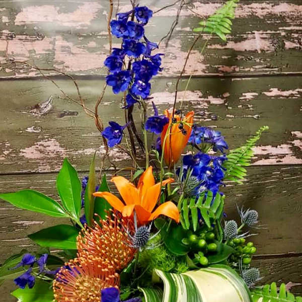 Tropical floral arrangement with orange lilies and blue flowers in a low container