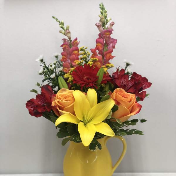 Colorful bouquet in a yellow pitcher vase with roses, lilies, and snapdragons