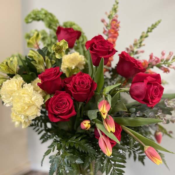 Bouquet of red roses, yellow carnations, and pink tulips in a glass vase
